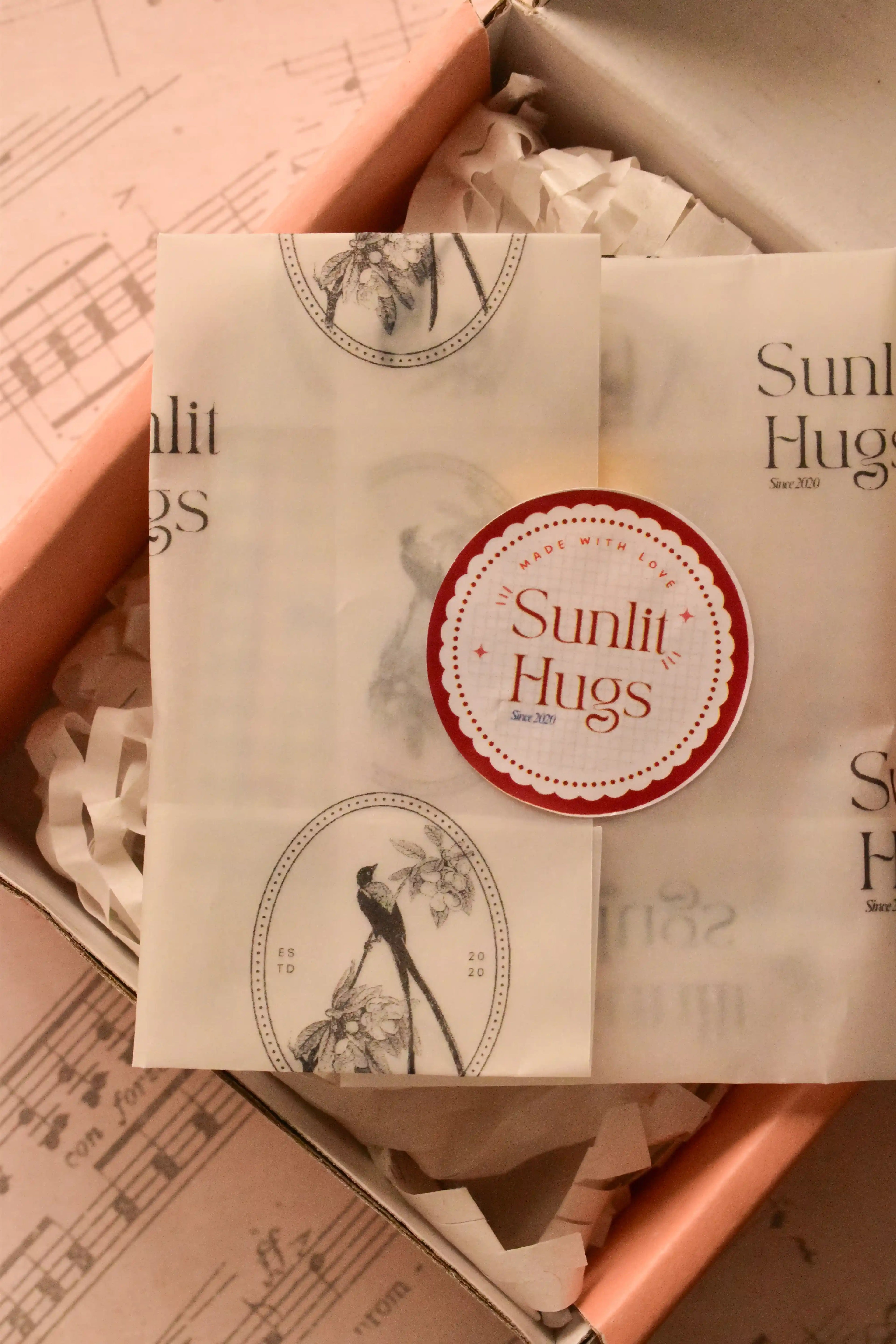 This image shows the beautiful presentation of the locket gift, wrapped in Sunlit Hugs tissue paper and sealed with a sticker, assuring customers of a warm, high-quality gift experience.