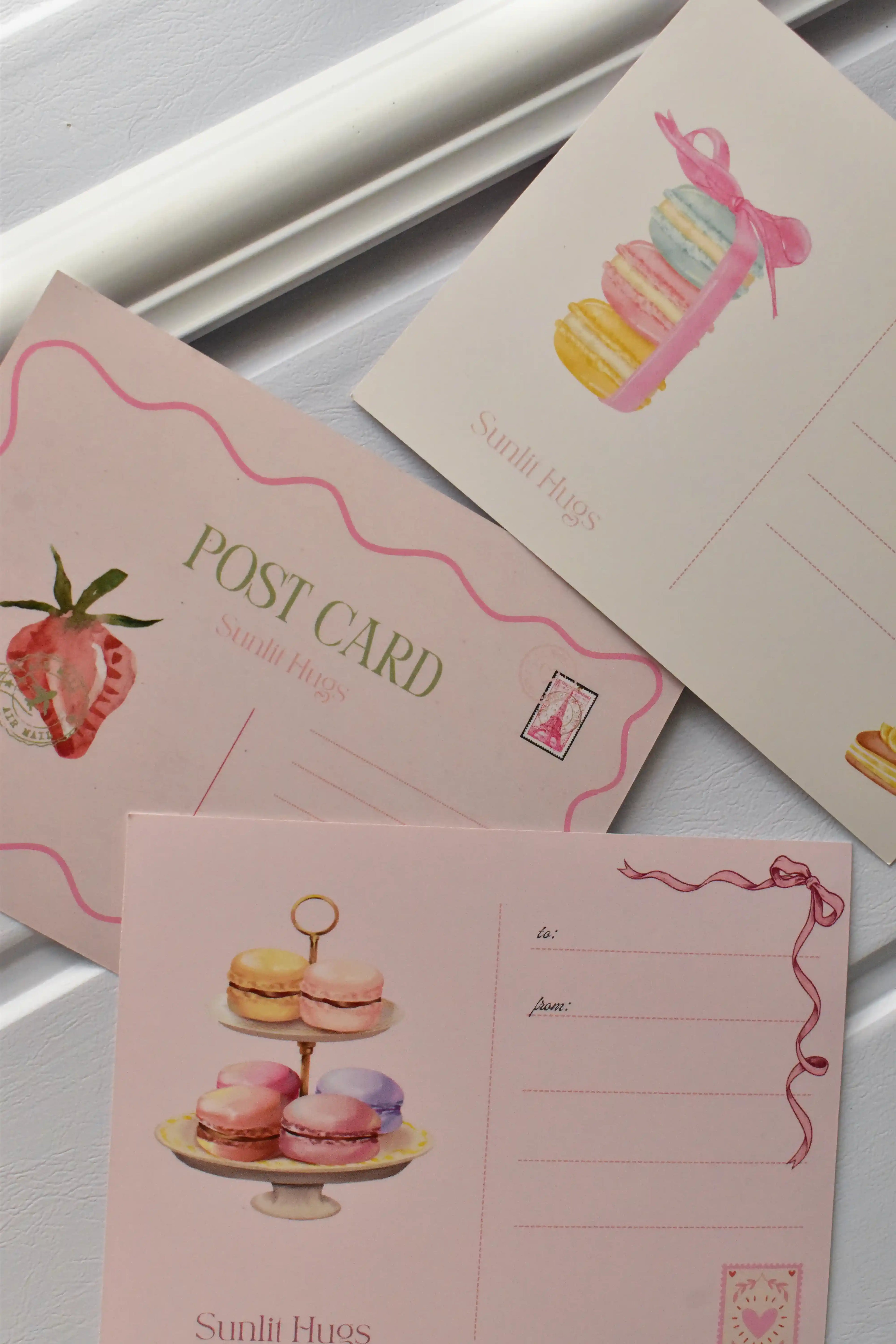 This angled image focuses on the reverse sides of the three postcards, showing the variety of address panel designs (macarons, strawberry, macaron tier) included in the set.