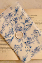 his image focuses on the tactile detail of the closure, showing the gentle seal and the intricate blue floral pattern that adds depth and whimsy to the old-world letter.