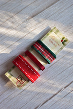 An angled view of the three Christmas ribbons (green plaid, thin red satin, and wide red stitched grosgrain) on their festive card stock label.