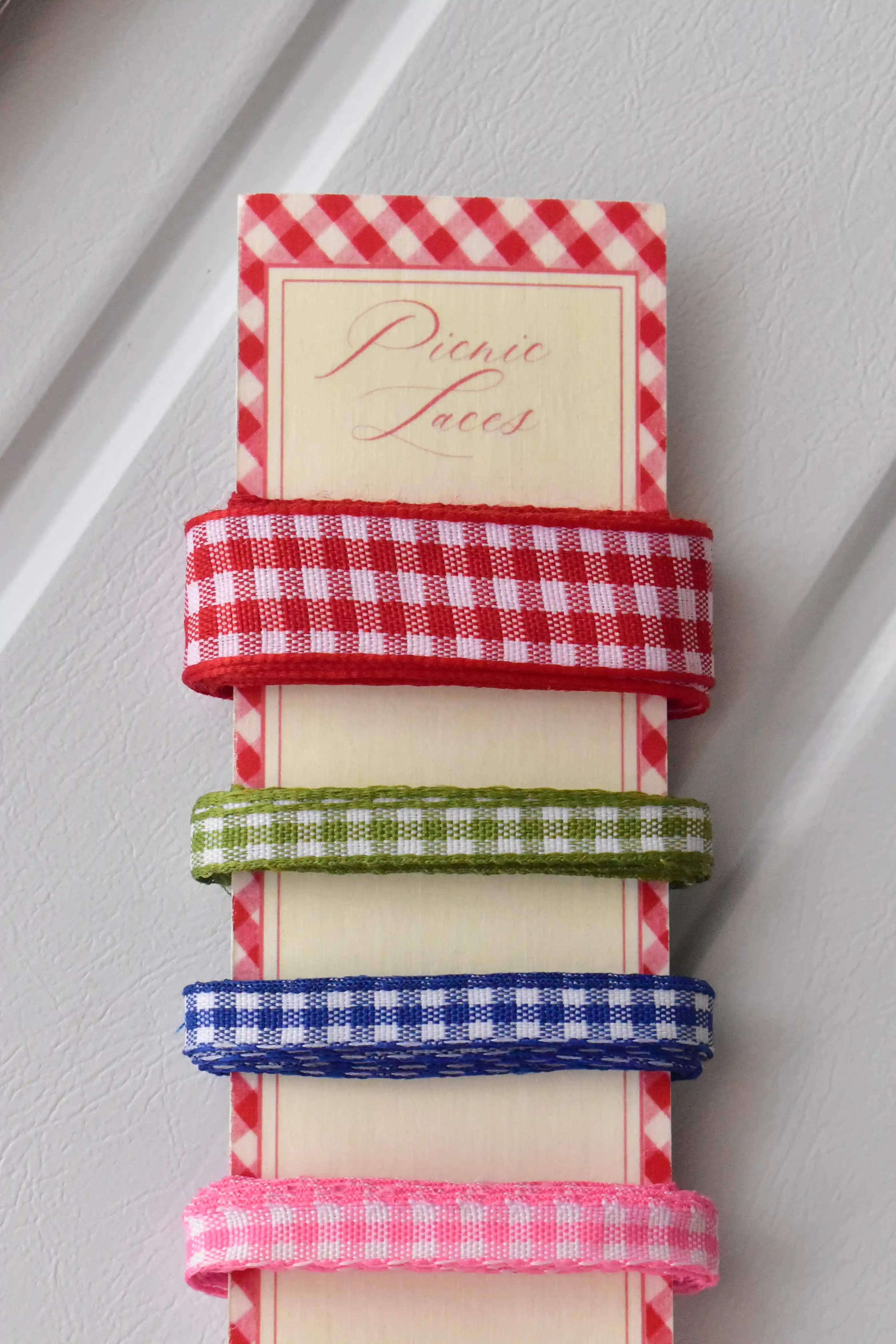 Vertical display of four narrow gingham ribbons in red, green, blue, and pink, set on the 'Picnic Laces' card.
