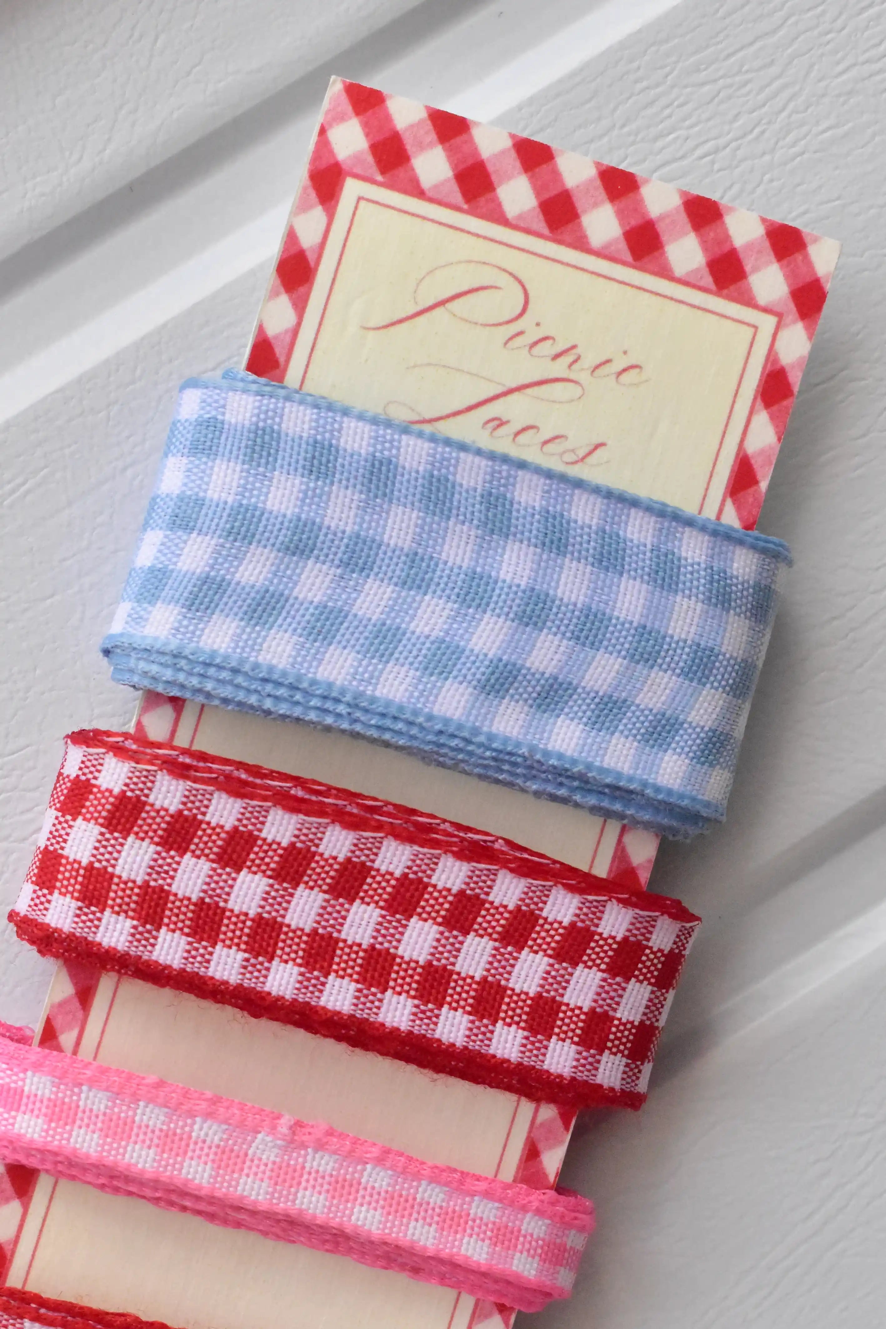 Close-up of the wide light blue, wide red, and narrow pink gingham ribbons wrapped around the top of the display card.