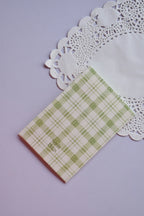 Close-up of the Sunlit Hugs logo subtly printed on the back of the green plaid, high-quality paper greeting card.