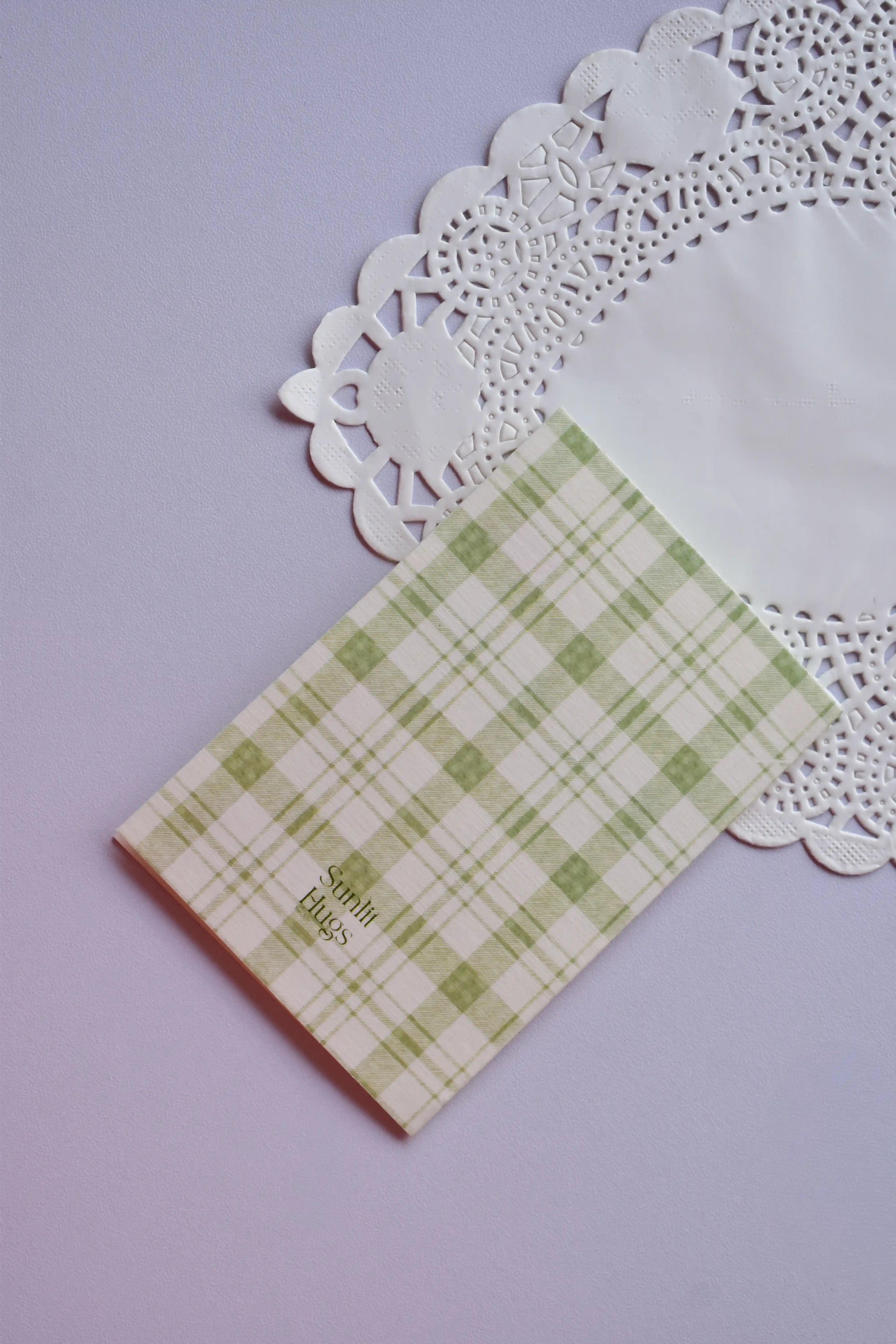 Close-up of the Sunlit Hugs logo subtly printed on the back of the green plaid, high-quality paper greeting card.
